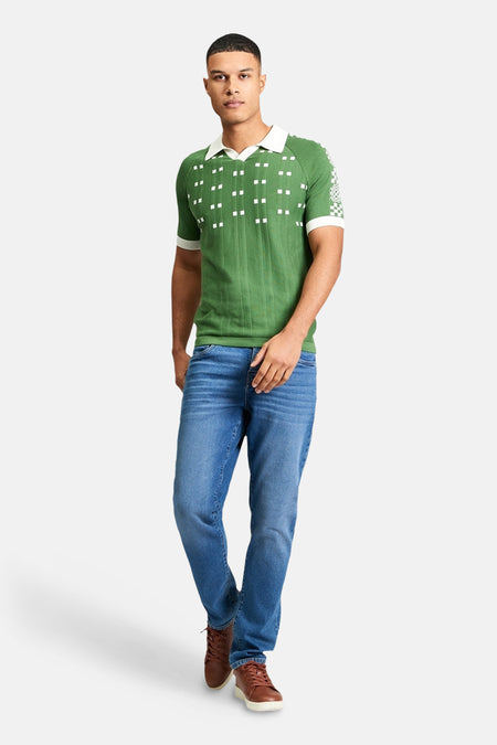 Groene polo van BEN SHERMAN, met witte vierkantjes, korte mouwen met witte boorden, gecombineerd met blauwe jeans en bruine schoenen.