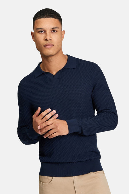 Blauwe pull van BEN SHERMAN, met een subtiel textuurpatroon en lange mouwen, gedragen met een beige broek.
