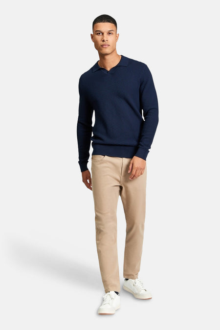 Blauwe trui van BEN SHERMAN, met een subtiel textuurpatroon en lange mouwen, gecombineerd met een beige broek en witte sneakers.
