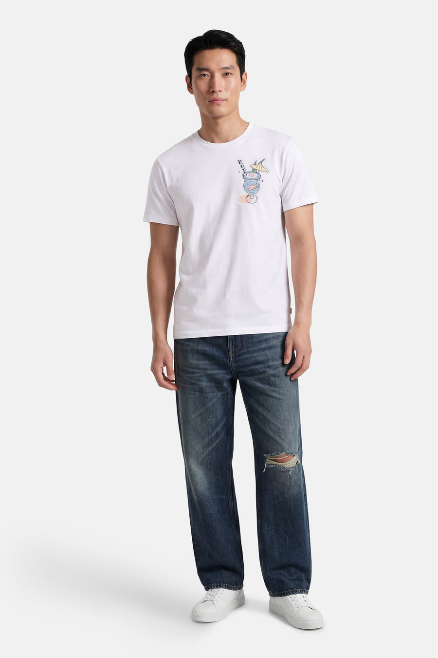 T-shirt blanc BEN SHERMAN avec imprimé verre à cocktail avec poisson, paille et parasol, porté par un homme avec un jean délavé et des baskets blanches.