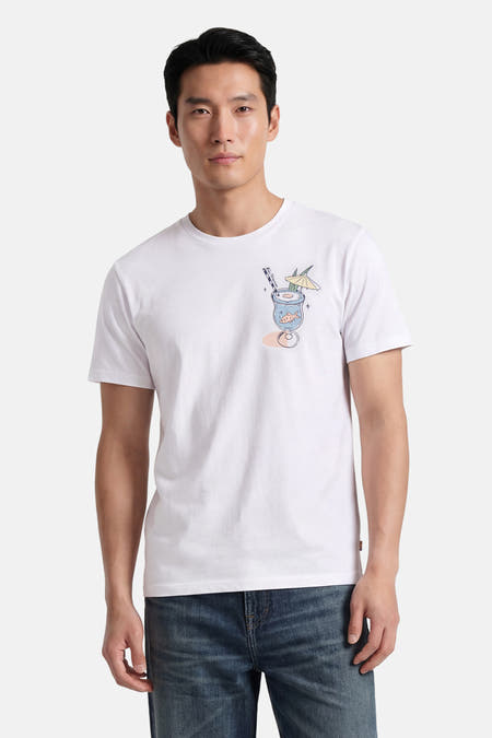 T-shirt blanc BEN SHERMAN avec un imprimé poitrine d'un verre à cocktail avec 'Be Summer', poisson rouge, paille et parasol, porté par un homme.