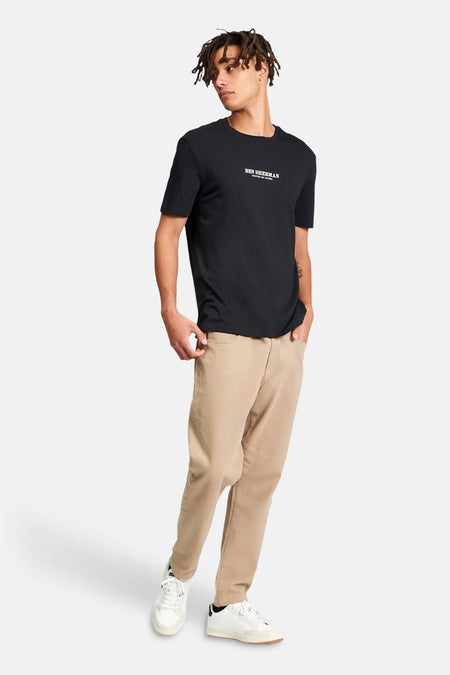 Zwart T-shirt van BEN SHERMAN, met korte mouwen, gecombineerd met een beige broek en witte sneakers.