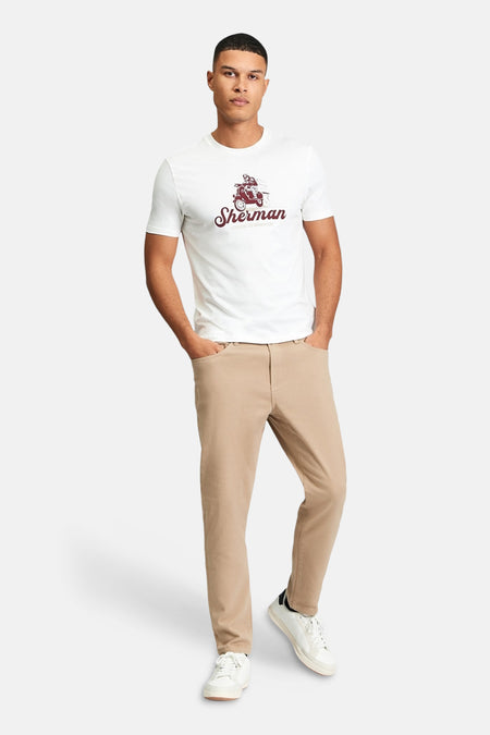 Wit T-shirt van BEN SHERMAN met een rode scooter print, gedragen met een bruine broek en witte sneakers.
