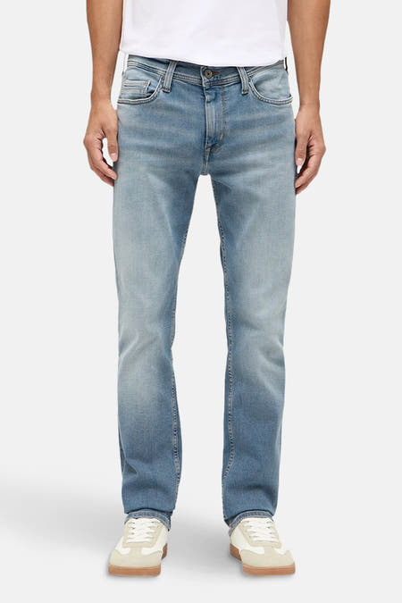 Jean slim en denim bleu clair de MUSTANG, porté avec un T-shirt blanc et des baskets crème.