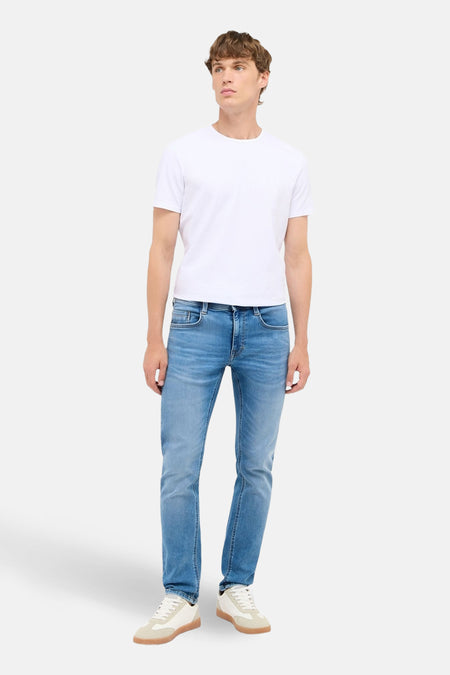 Jean slim fit en denim bleu clair de MUSTANG, avec t-shirt blanc et baskets couleur crème.