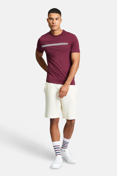 Ecru korte broek van Ben Sherman, gedragen met een bordeauxrood T-shirt en gestreepte sokken en witte sneakers.
