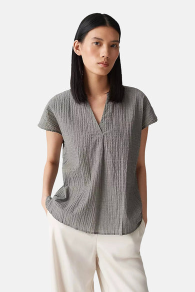 Blouse kaki à manches courtes d'OPUS, avec un col V et une subtile texture plissée, portée avec un pantalon crème.