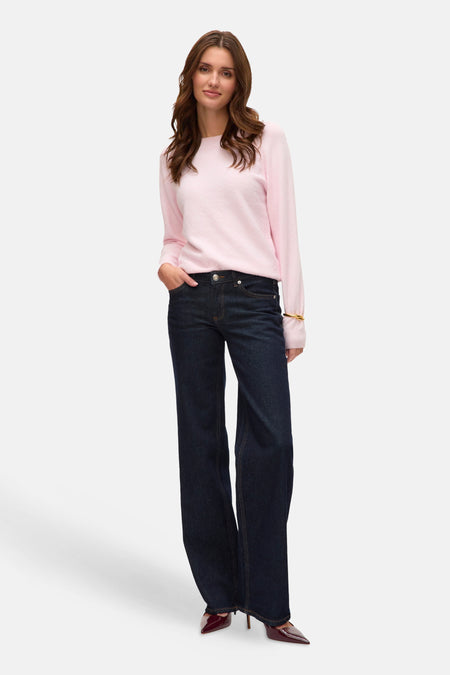 Vrouw in roze trui, blauwe jeans en bordeauxrode pumps.