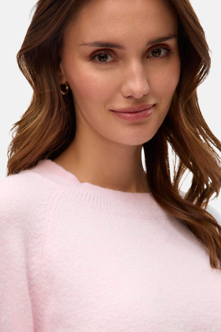 Vrouw in roze gebreide trui met bruin haar en gouden oorbellen.