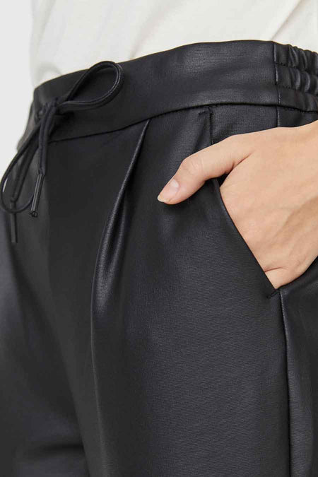 Pantalon noir en similicuir de VERO MODA® avec cordon de serrage, taille élastique et plis, avec une main dans la poche.