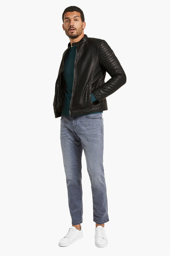 Man met zwart leren jack, groene trui, grijze jeans en witte sneakers.