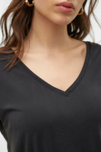 T-shirt V-hals noir de VERO MODA, coupé près du corps, avec des boucles d'oreilles dorées et des cheveux bruns.