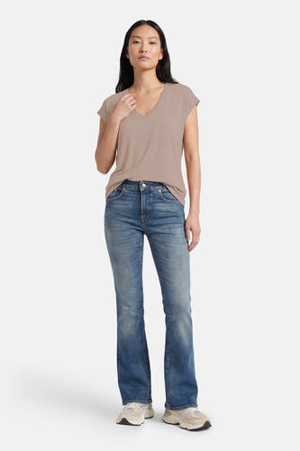 Beige T-shirt met korte mouwen van VERO MODA®, gedragen met blauwe jeans en crèmekleurige sneakers.