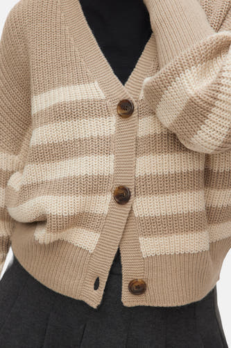 Cardigan beige de VERO MODA, avec un motif à rayures et des boutons bruns, porté sur une chemise noire et une jupe grise foncée.