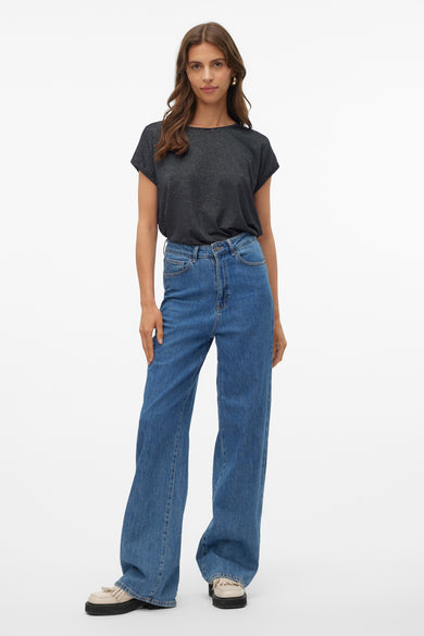 T-shirt noir à manches courtes de VERO MODA, avec une texture scintillante, associé à des jeans larges et des chaussures à plateforme.