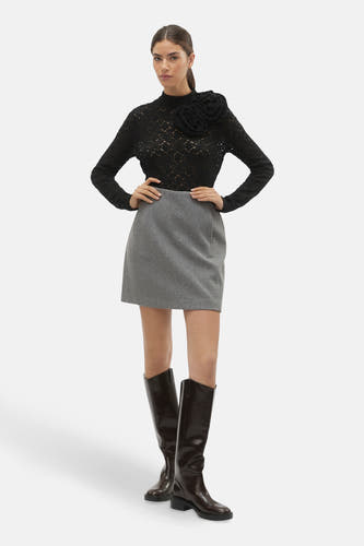 Jupe grise courte de Vero Moda, associée à une chemisier noire avec des détails floraux et des bottes brunes hautes.