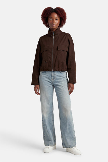 Manteau marron OPUS, à manches longues et poches, combiné avec un jean bleu et des baskets blanches.