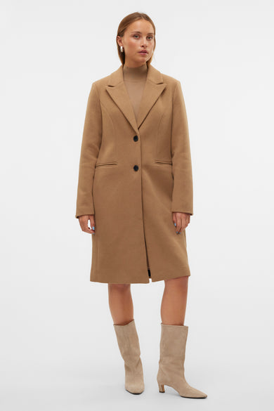 Manteau long marron de Vero Moda avec des boutons noirs, porté avec un gilet beige et des bottes en cuir de Suède.