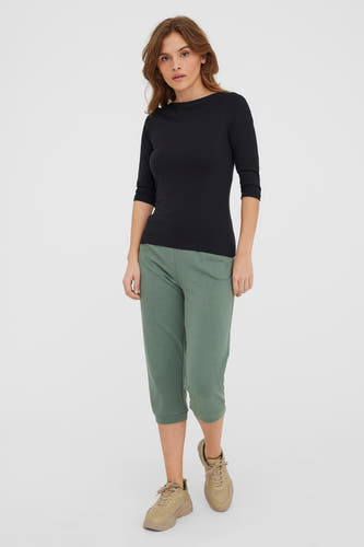 T-shirt noir à manches longues de VERO MODA®, porté avec un pantalon trois-quarts vert et des baskets beige.