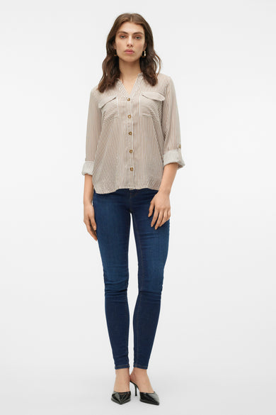 Chemise brune à carreaux de Vero Moda avec des manches longues, des poches poitrine et des manches retroussées, portée avec un jeans foncé et des bottes noires.