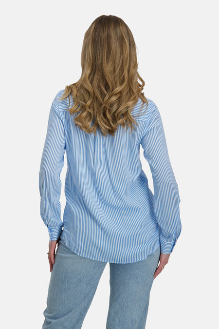 Een vrouw van achteren gezien in een blauw-wit gestreept overhemd en een jeans.