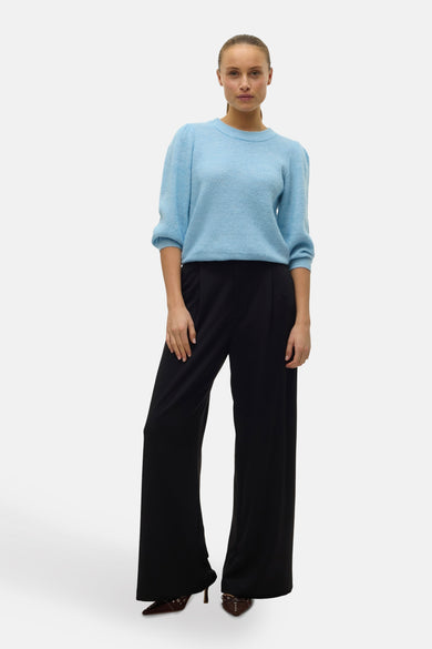 Pull bleu à col rond de Vero Moda, avec manches bouffantes et porté avec un pantalon noir évasé.