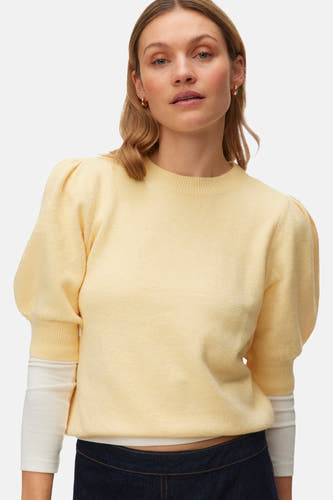Pull jaune à col rond de Vero Moda, avec manches bouffantes et porté sur une chemise blanche, combiné avec une jupe bleu foncé.