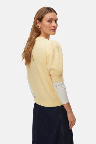 Gele trui met ronde hals van Vero Moda, met pofmouwen en gedragen over een wit shirt, gecombineerd met een donkerblauwe rok.