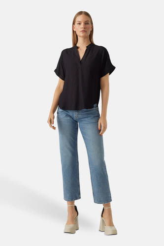 Zwarte blouse van VERO MODA®, met korte mouwen en een losse pasvorm, gecombineerd met blauwe jeans en beige hakken.