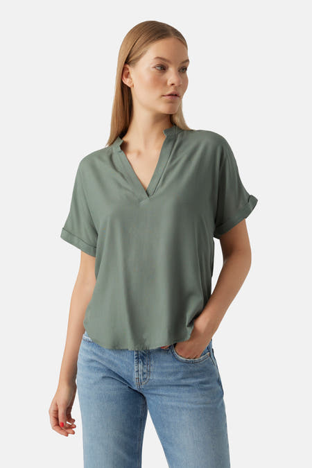 Blouse verte avec manches courtes de VERO MODA, avec un col en V et des manches roulées, associée à des jeans bleus.