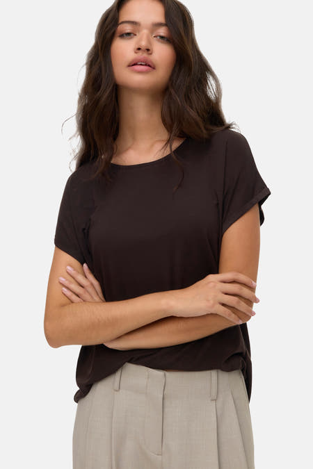 T-shirt brun à manches courtes de VERO MODA, porté avec un pantalon beige et les bras croisés.