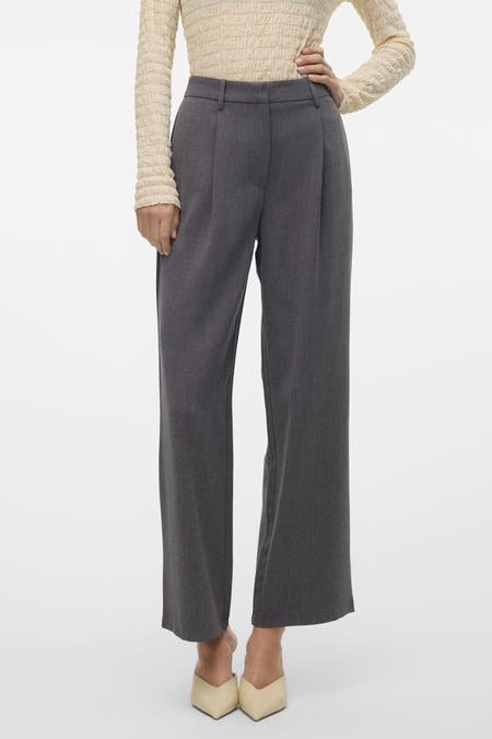 Pantalon gris de VERO MODA, pinces tombantes, taille haute, associé à une chemise blanche et des chaussures pointues.