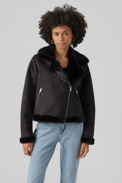 Manteau court noir de VERO MODA, avec fourrure imitée sur la capuche, les manches et le col, porté avec un pantalon de cuir.