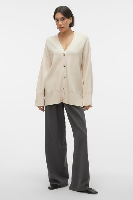 Beige gilet van VERO MODA®, gedragen over grijze broeken en zwarte schoenen.

