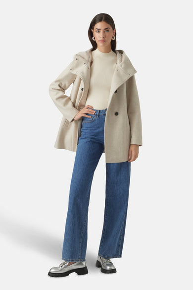 Manteau court beige de VERO MODA®, avec capuche, associé à une chemise tricotée et des jeans.