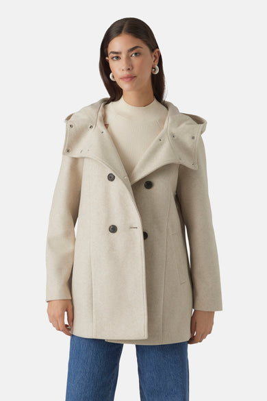 Manteau court beige de Vero Moda avec capuchon et fermeture à double bouton, porté avec un pull tricoté et des jeans.