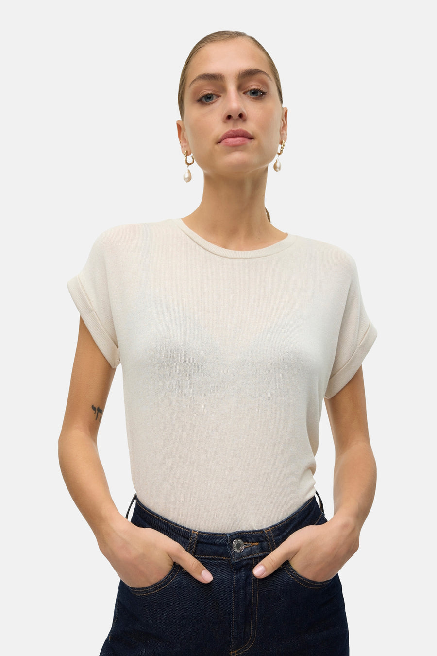 T-shirt beige à manches courtes de VERO MODA®, avec des manches retroussées et un jeans foncé les mains dans les po po.