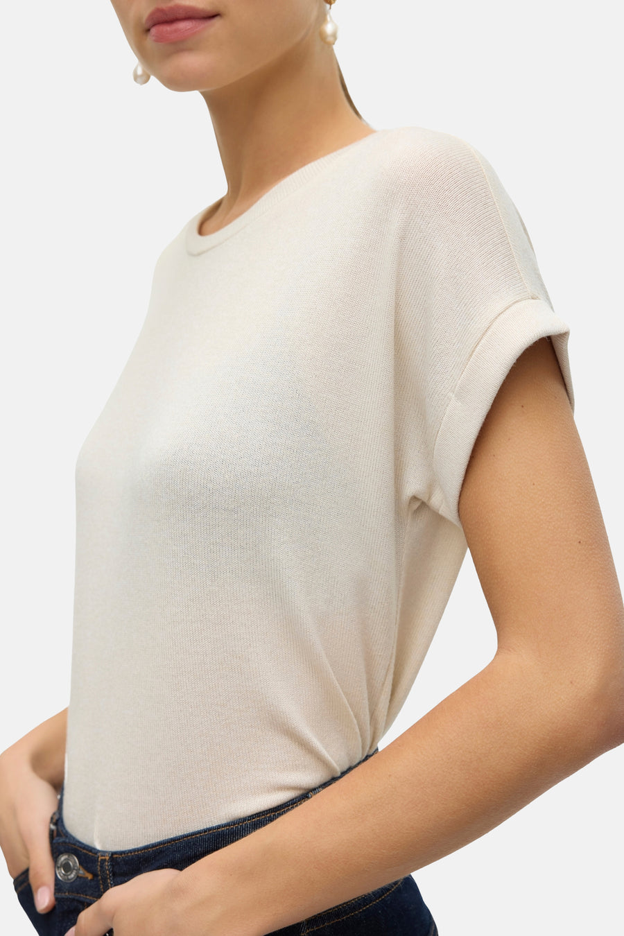 T-shirt beige à manches courtes de VERO MODA, avec des manches retroussées, porté avec un jeans bleu marine.