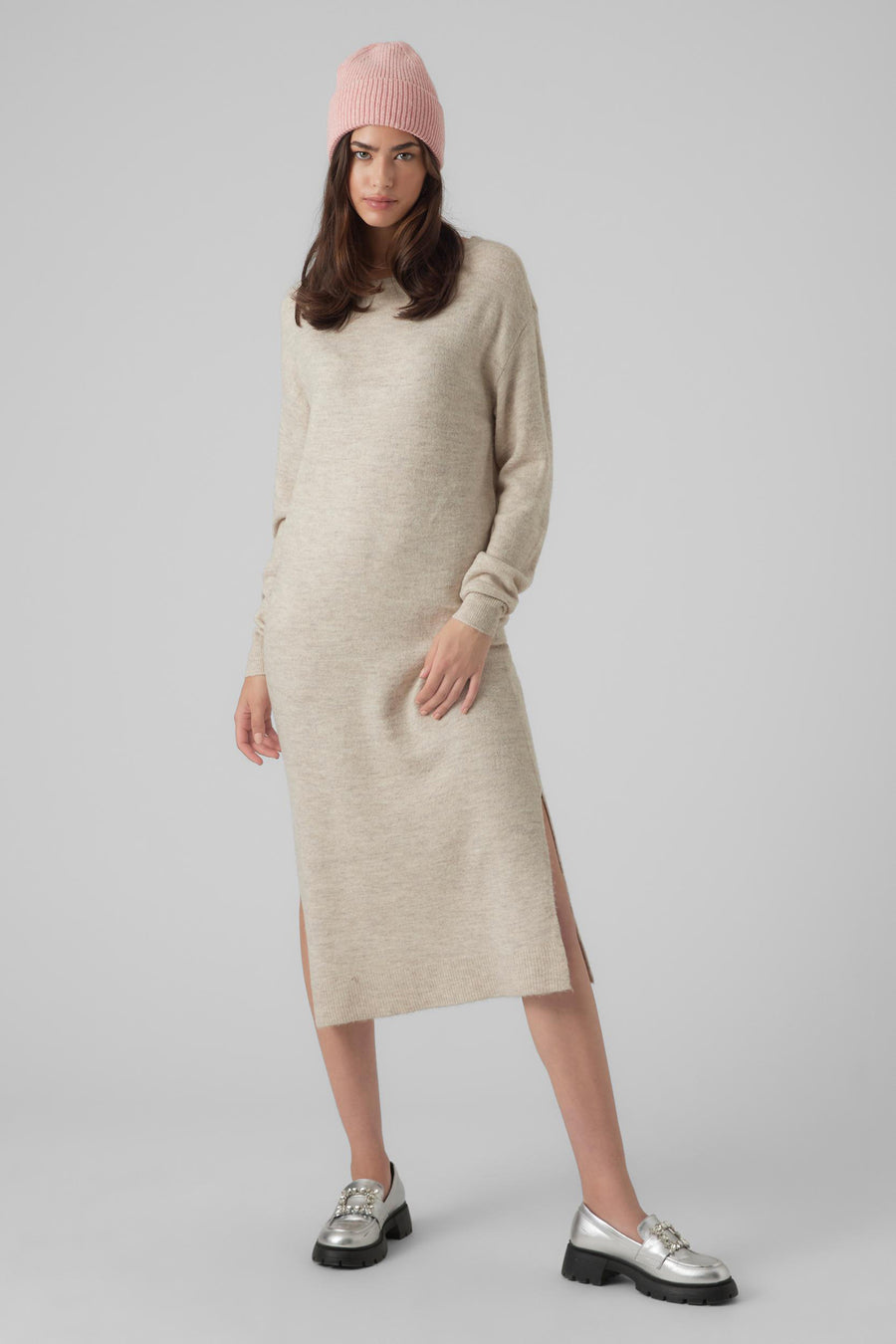 Manteau beige à longues manches de VERO MODA, avec une fente sur le côté et porté avec un chapeau rose et des chaussures argentées.