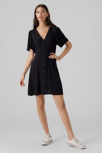 Robe noire à manches courtes de Vero Moda, avec une fermeture à boutons et portée avec des baskets blanches.