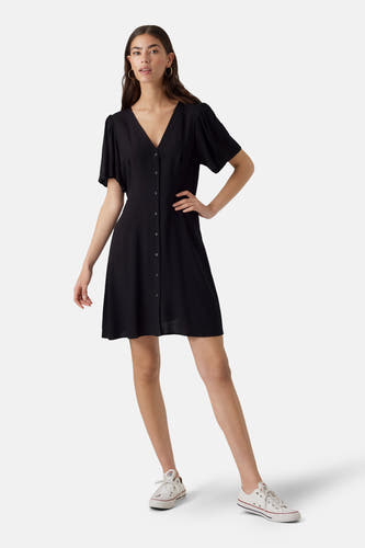 Robe noire à manches courtes de VERO MODA®, avec une fermeture à boutons et portée avec des baskets blanches.