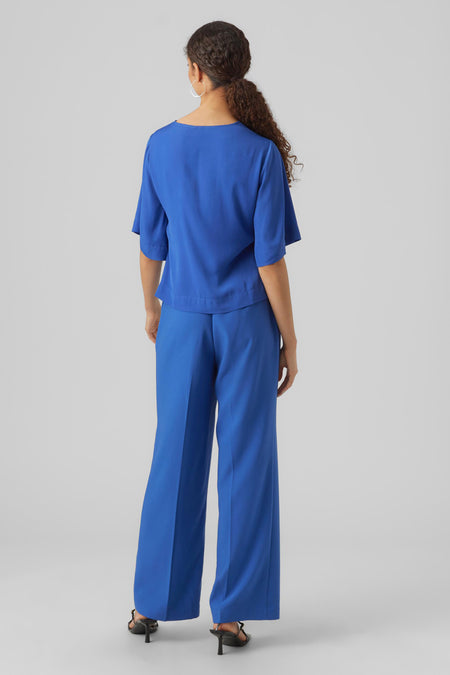 Blauwe blouse met driekwart mouwen van VERO MODA, gezien van achteren, gecombineerd met bijpassende pantalon en hakken.
