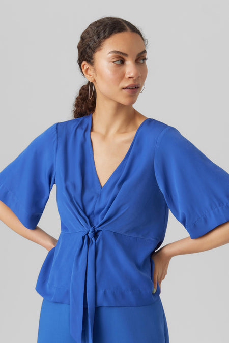 Blouse bleue de VERO MODA, avec détail de boutons et manches courtes, associée à un pantalon bleu.