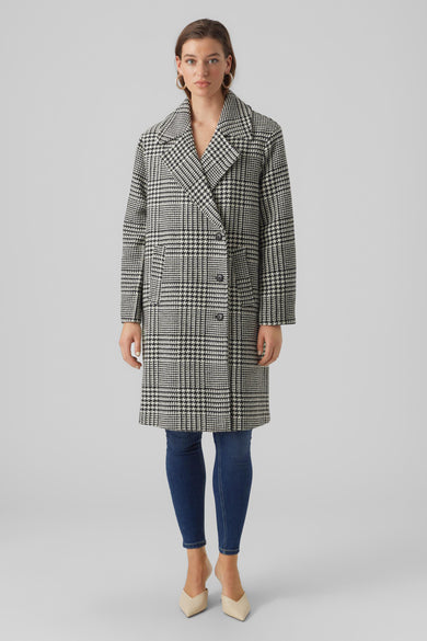 Manteau noir et blanc long de VERO MODA® avec un motif de capuche, porté avec un jeans bleu et des chaussures beige.