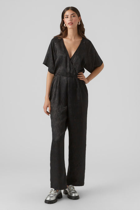Combinaison noire de VERO MODA, avec des manches courtes et un modèle wrap, associée à des chaussures argentées avec des boucles décoratives.