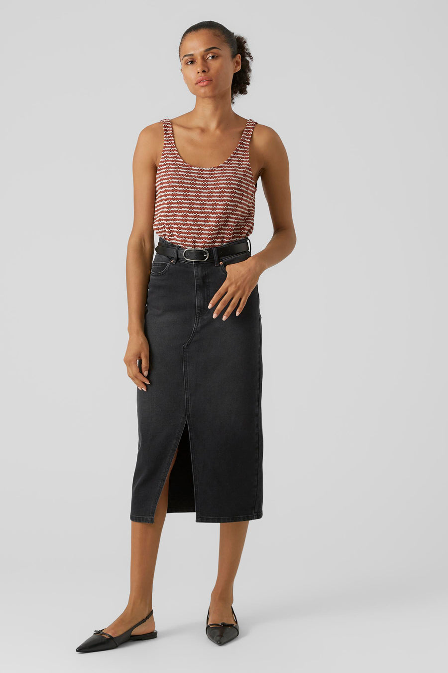 Zwarte rok van VERO MODA, met split aan de voorkant, gecombineerd met een gestreepte top en riem.
