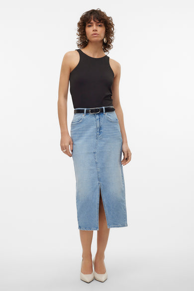 Jupe en denim bleu clair de VERO MODA, avec une fente et associée à un top noir et des chaussures blanches.