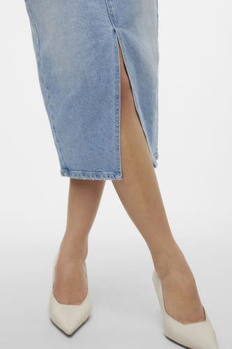 Jupe en denim bleu clair de Vero Moda avec une fente, associée à des escarpins blancs.