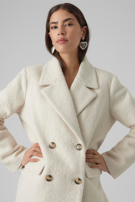 Veste courte écrue de VERO MODA® avec double rangée de boutons foncés et texture brossée, vue de face du modèle avec les mains sur les hanches