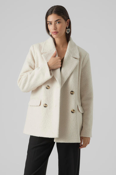 Bontjas couleur écru de VERO MODA® avec double rangée de boutons dorés et poches, portée avec un pantalon noir